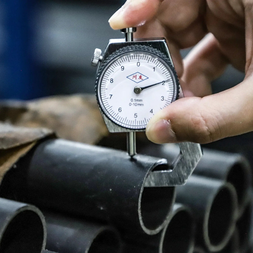 Measuring thickness of metal pipe with a dial gauge in a workshop setting.